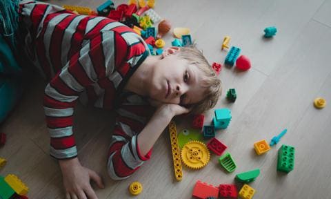 Niño aburrido, tirado en el suelo con juguetes a su alrededor
