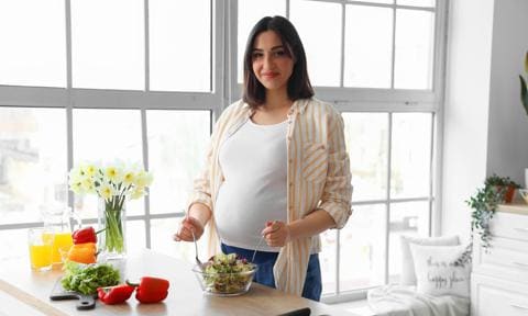 Mujer embarazada haciendo una ensalada en la cocina
