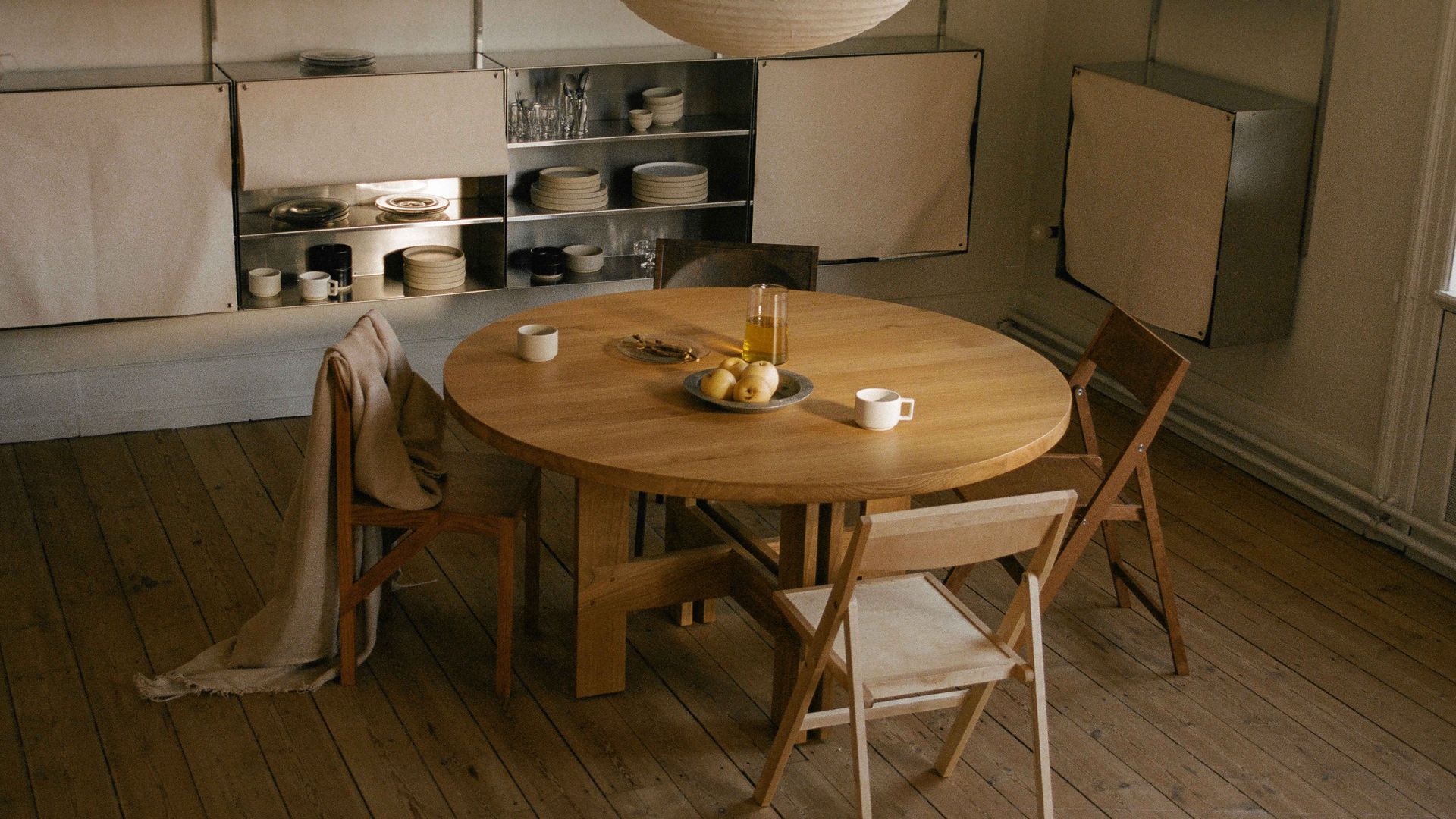 Comedor con mesa redonda XL, lámpara de techo, sillas de madera y estantería con puertas de tela