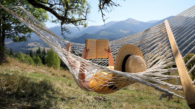 mujer en una hamaca en medio de la naturaleza leyendo un libro