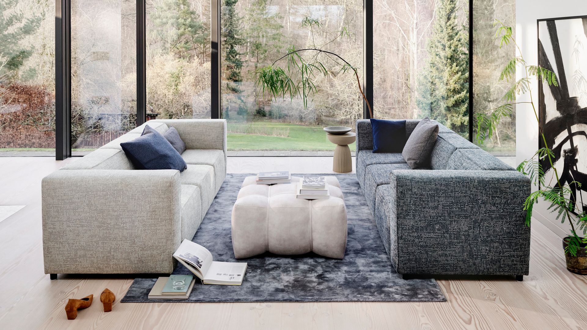 Salón con dos sofás enfrentados, uno blanco y otro gris, mesa de centro tapizada y alfombra gris