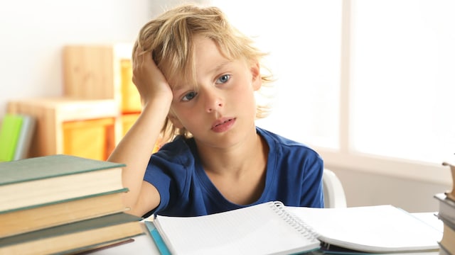 Niño con cara de cansado y tristeza sentado delante de los libros