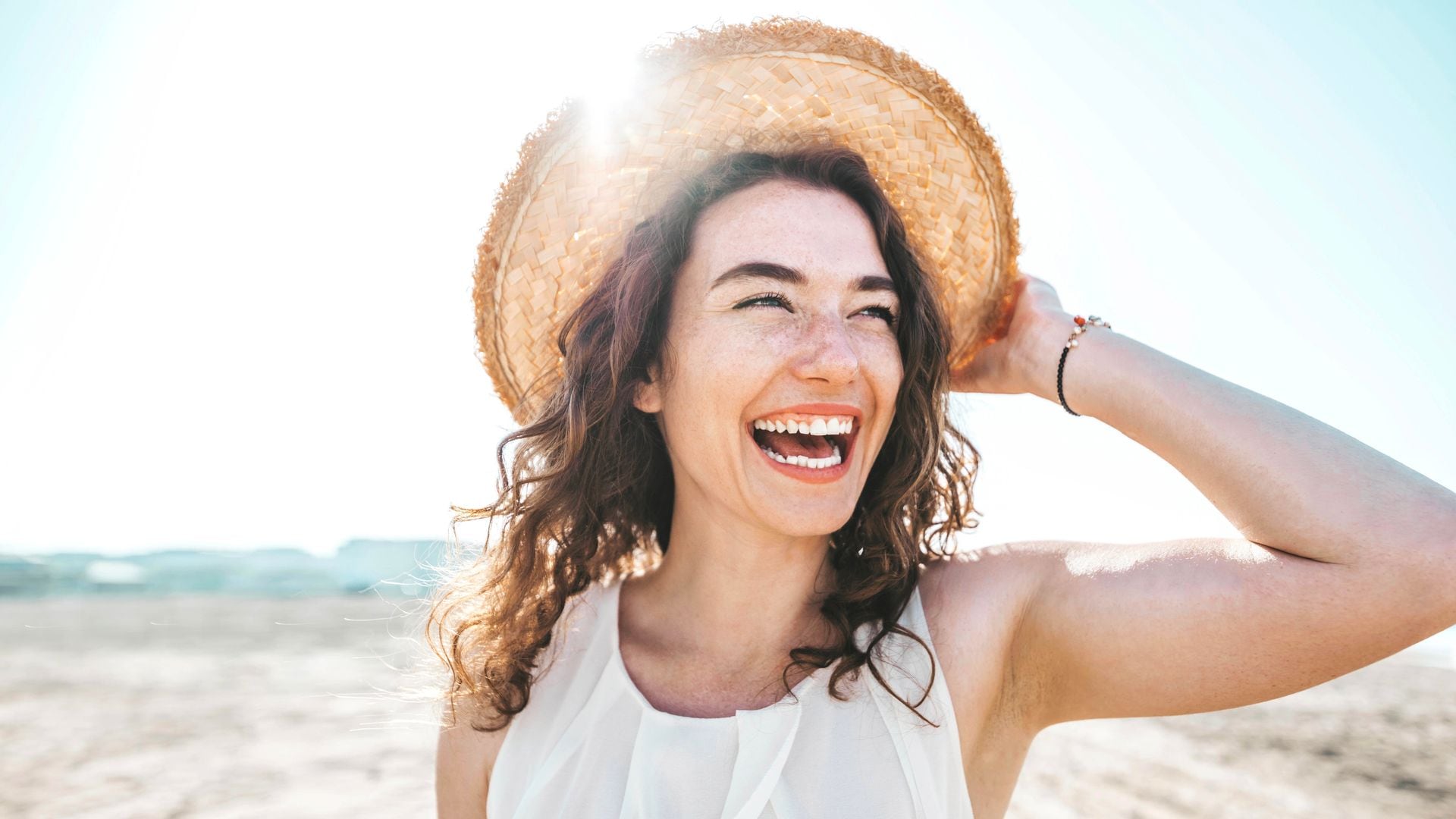 mujer sonriente en la playa con un sombrero de paja