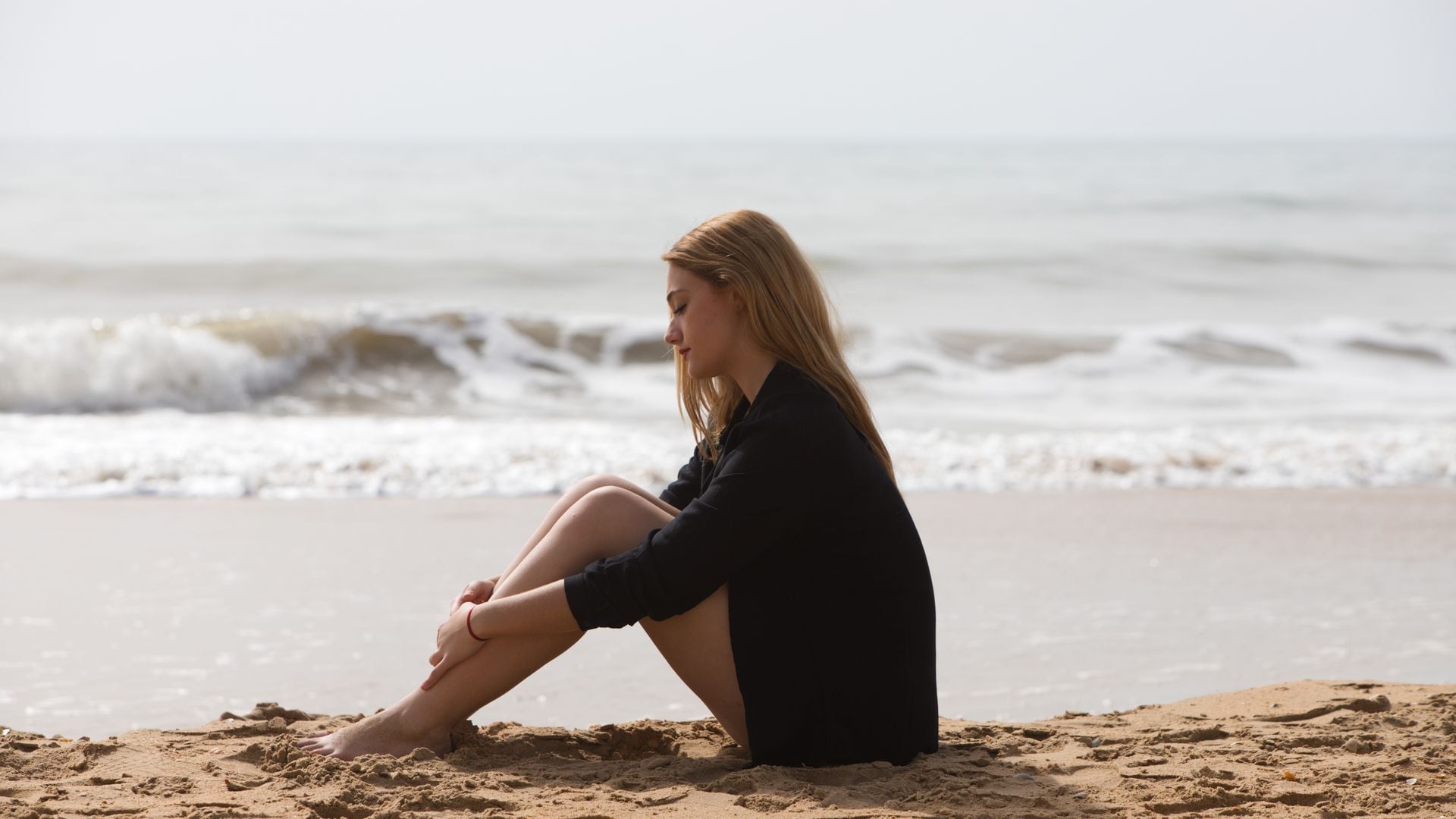 Mujer joven pensativa sentada en la arena de la playa con el mar de fondo