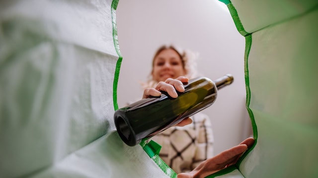 Imagen del interior de una bolsa de reciclaje verde de una mujer arrojando una botella de vidrio para reciclar