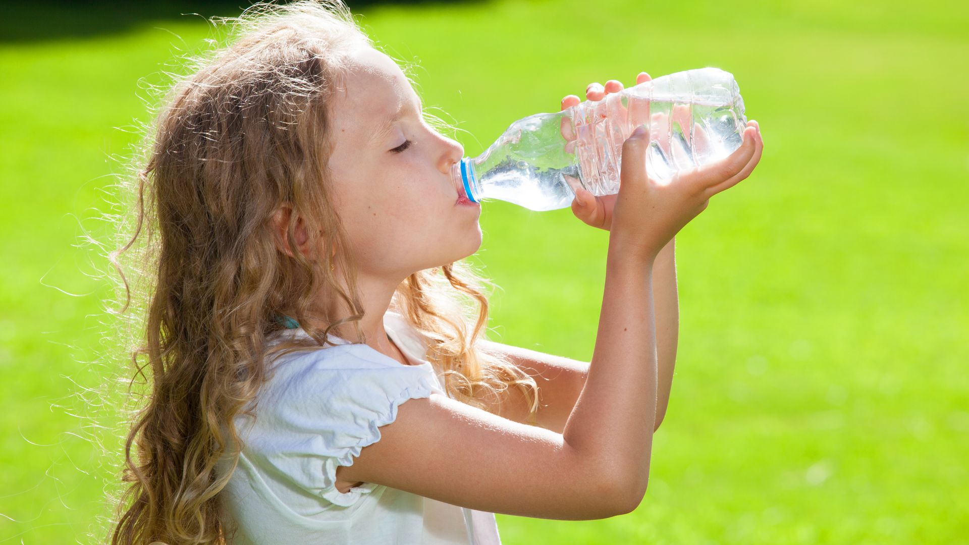 Niña pequeña al sol bebiendo una botella de agua