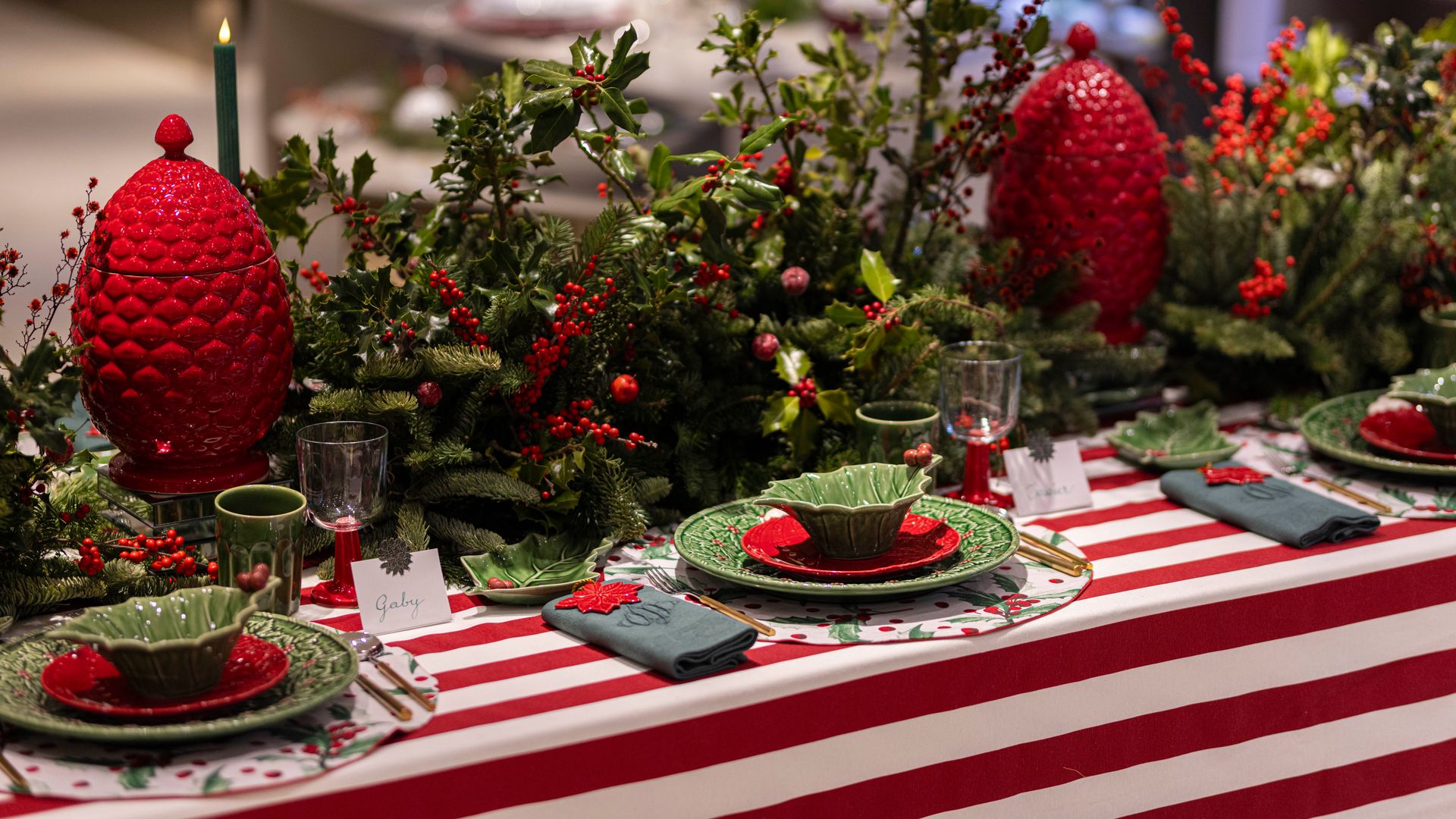 Mesa de Navidad con mantel de rayas rojas y blancas, vajilla verde y roja, centro con acebo y bolas rojas