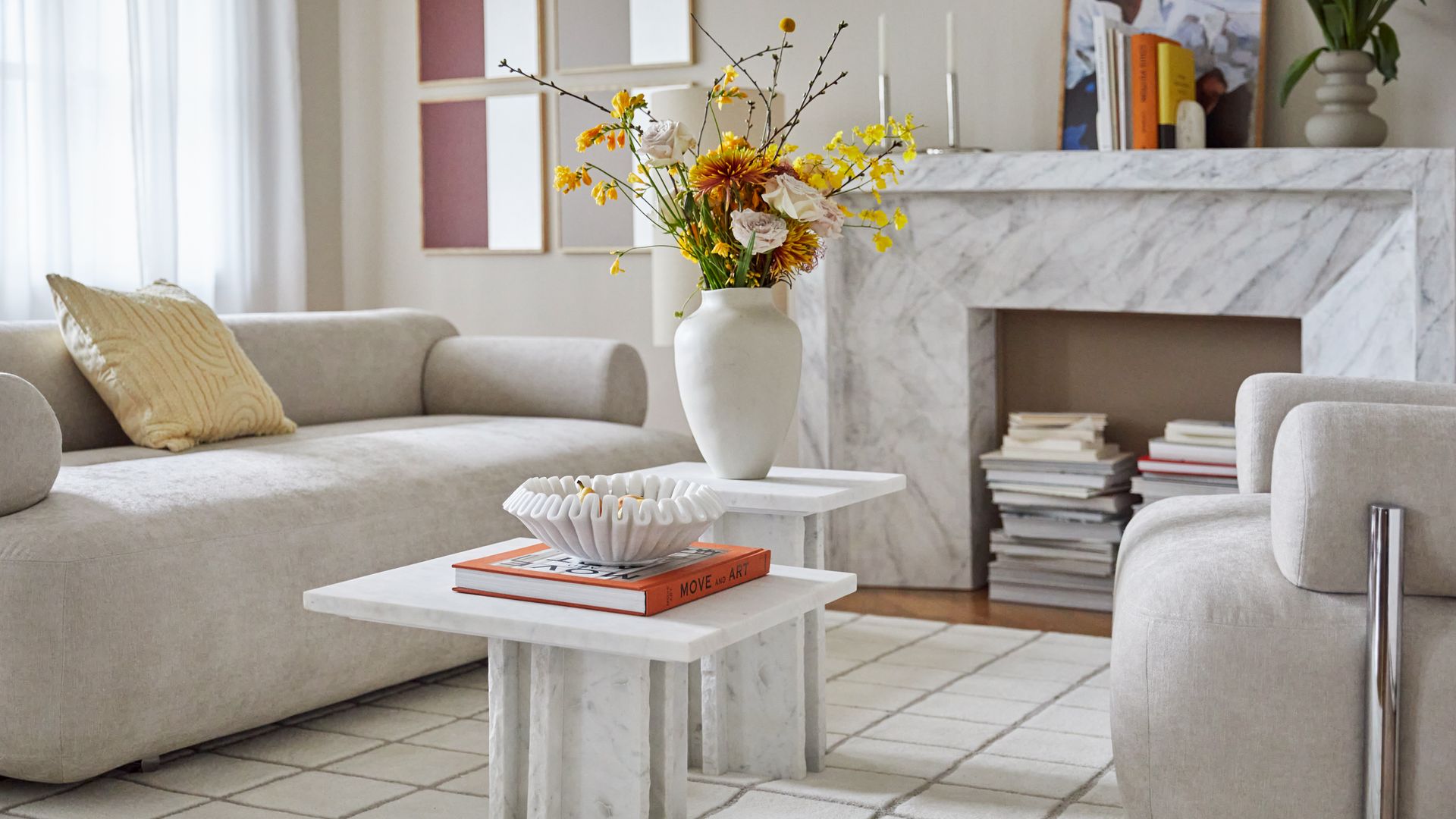 Salón con sofá blanco y chimenea de mármol a juego con la mesa de centro, jarrón con flores, libro y adorno