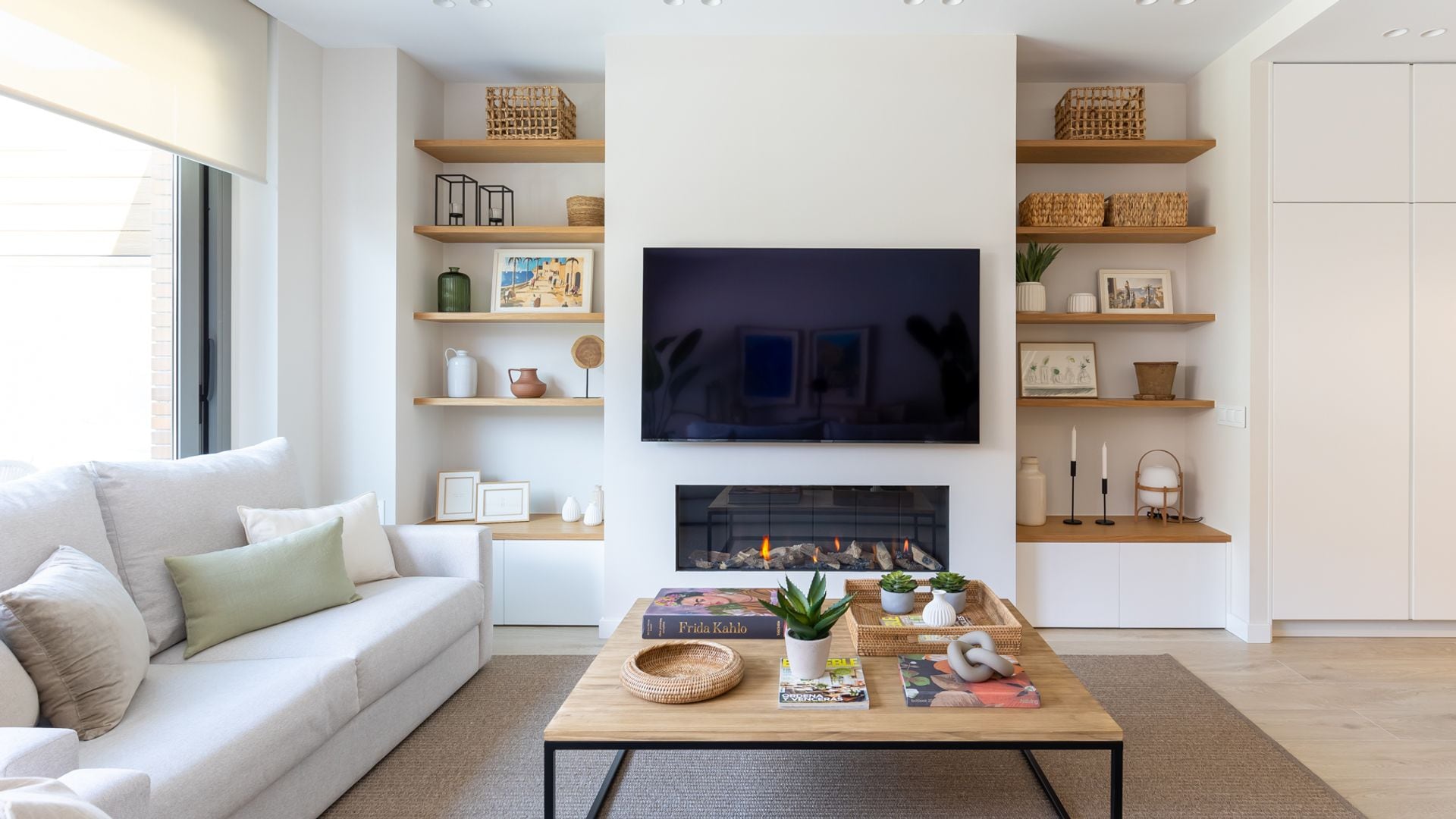 Salón con sofás blancos, chimenea, televisor colgado en la pared y dos estanterías gemelas a medida con baldas de madera