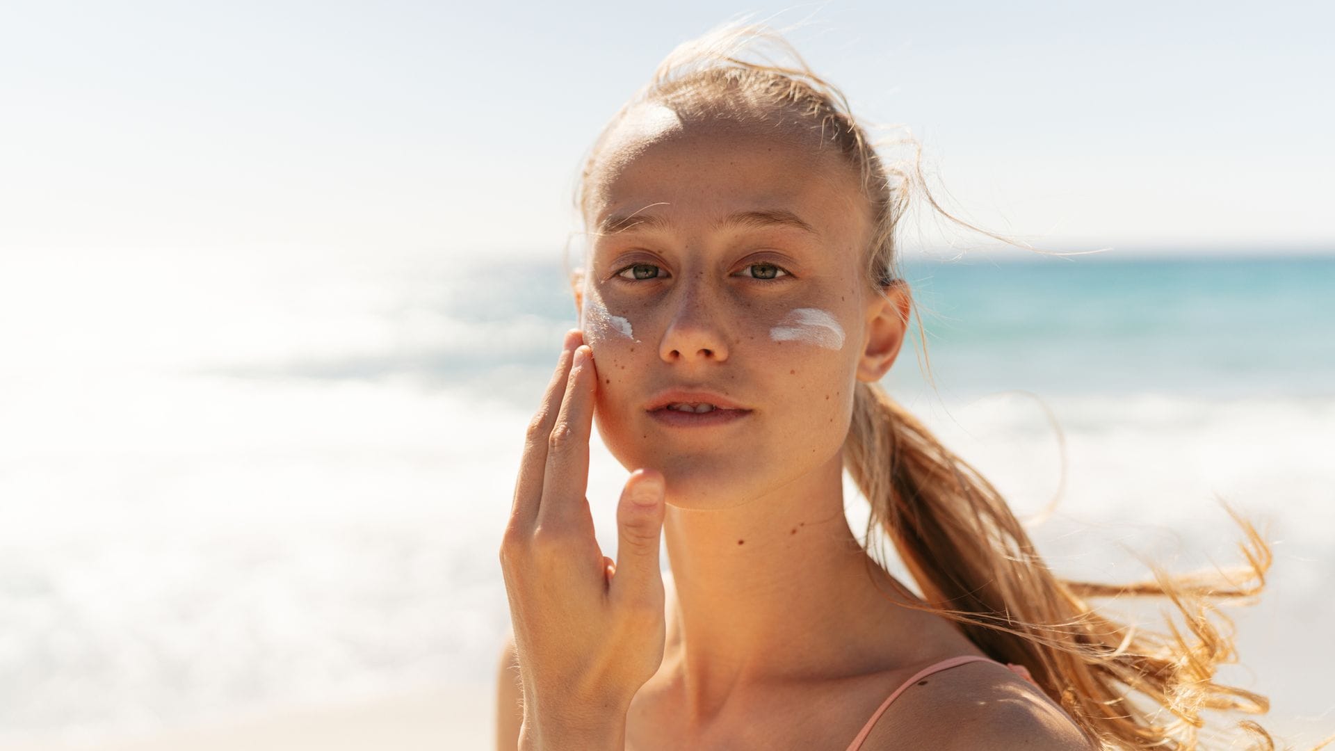 Mujer echándose crema en la cara en la playa