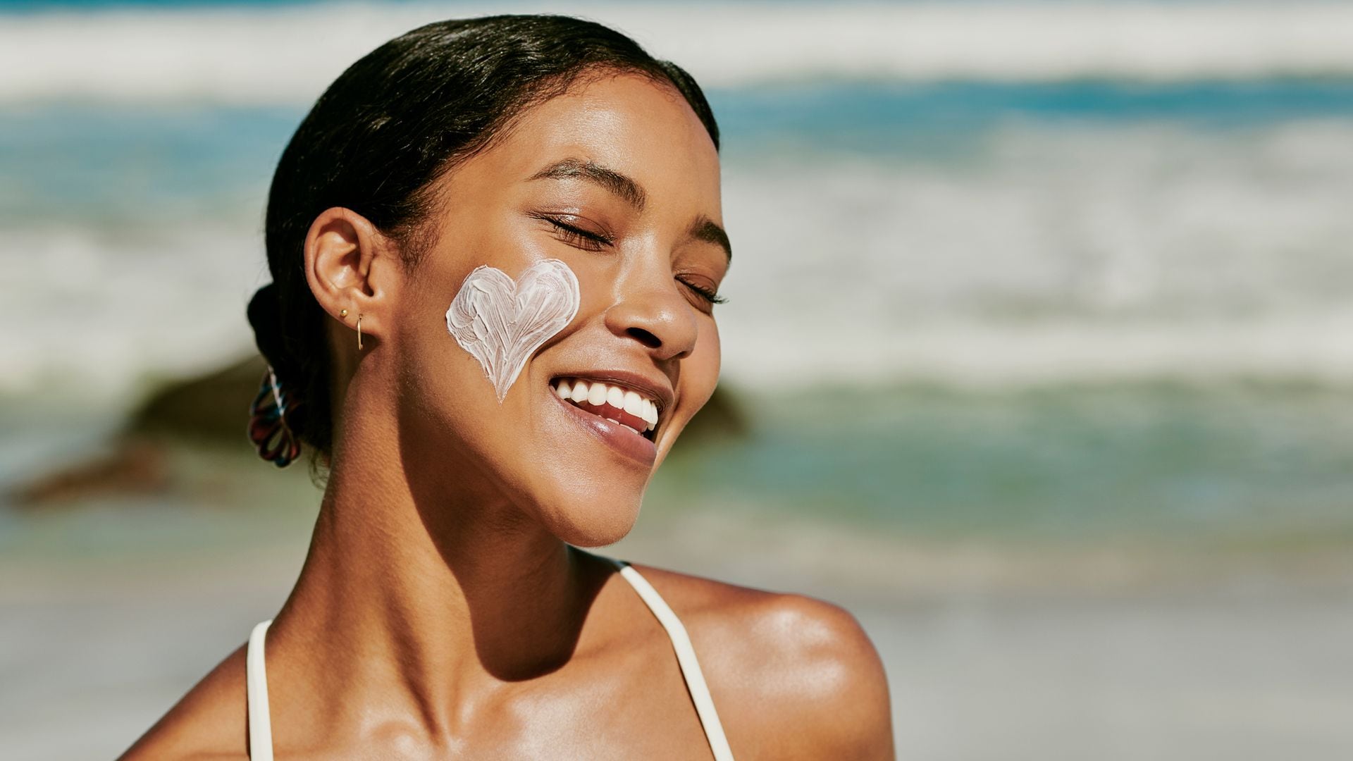 Mujer sonriendo en la playa con un corazón de crema solar facial