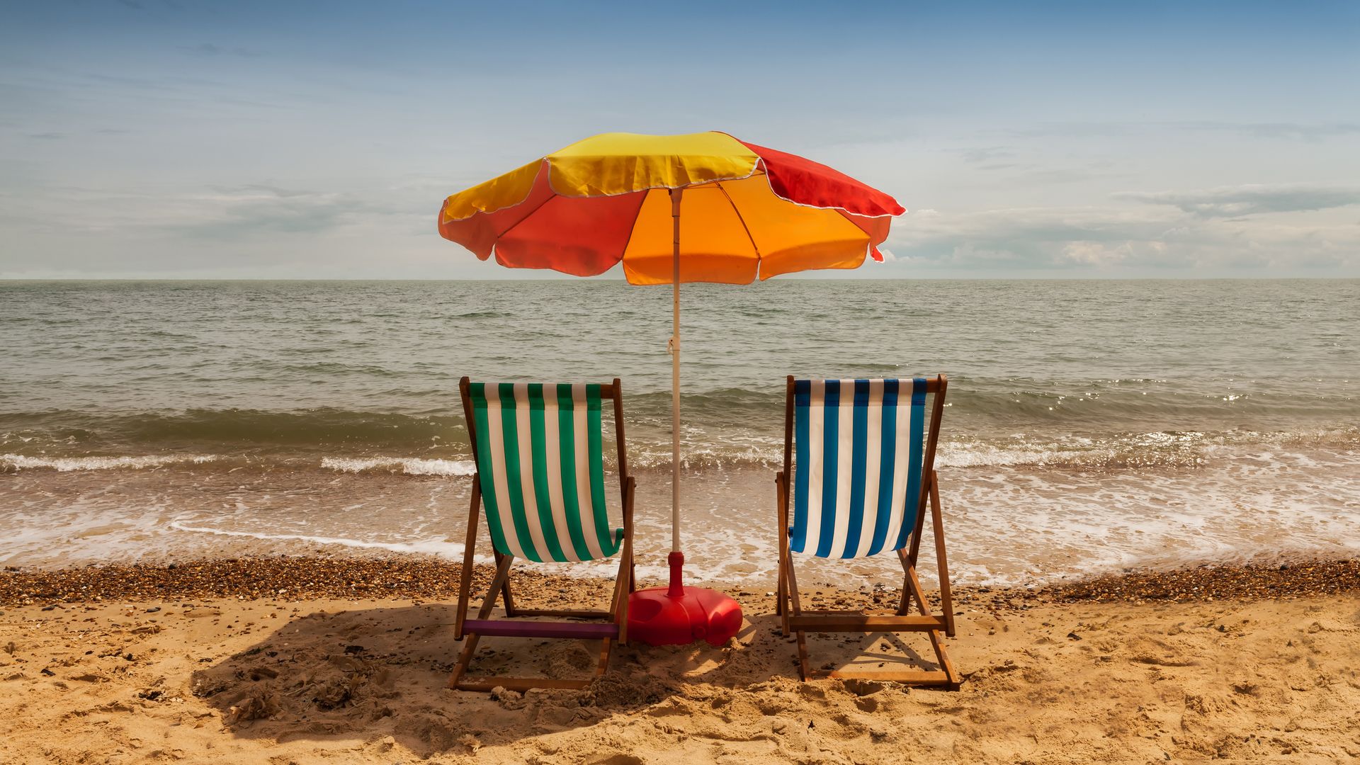 Clacton, Essex, UK. June 28, 2014. Image shows two deck chairs and parasol on a sandy beach on a sunny summer day.