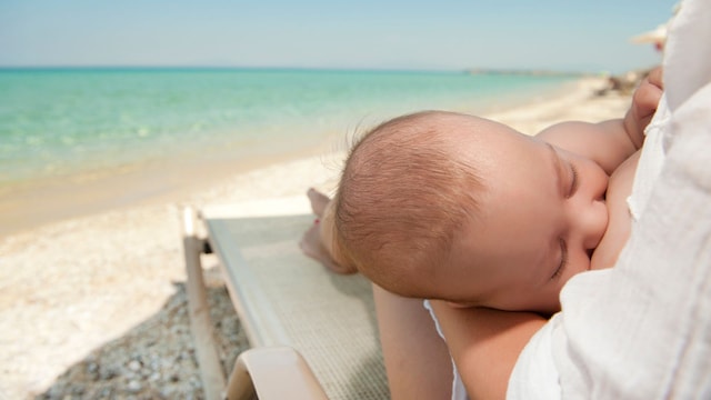 Bebé se alimenta del pecho de su madre en la playa