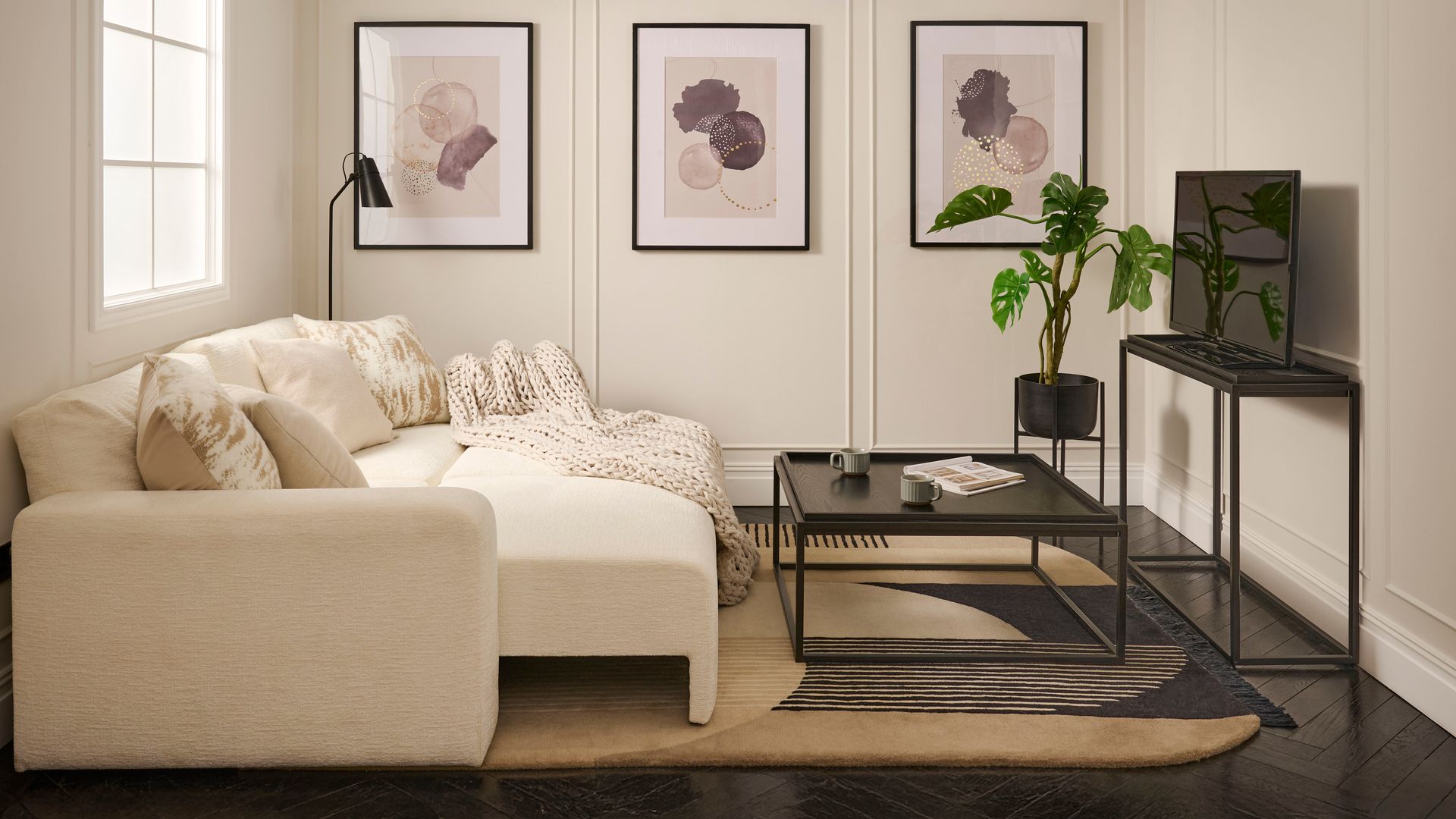 Salón con molduras en la pared, cuadros, sofá cama blanco, alfombra, mesa de centro y mueble para la televisión negros