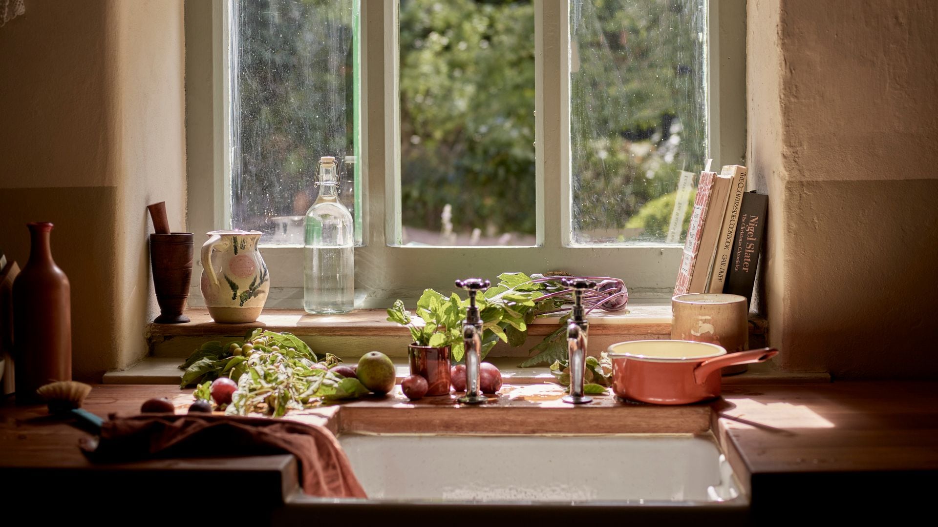 Cocina con fregadero antiguo, adorno de ganchillo en la ventana, accesorios de barro y plantas