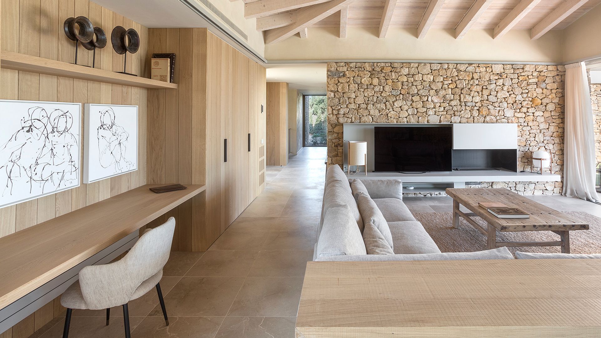 Salón con pared de piedra, mueble televisión, sofá blanco y escritorio de madera