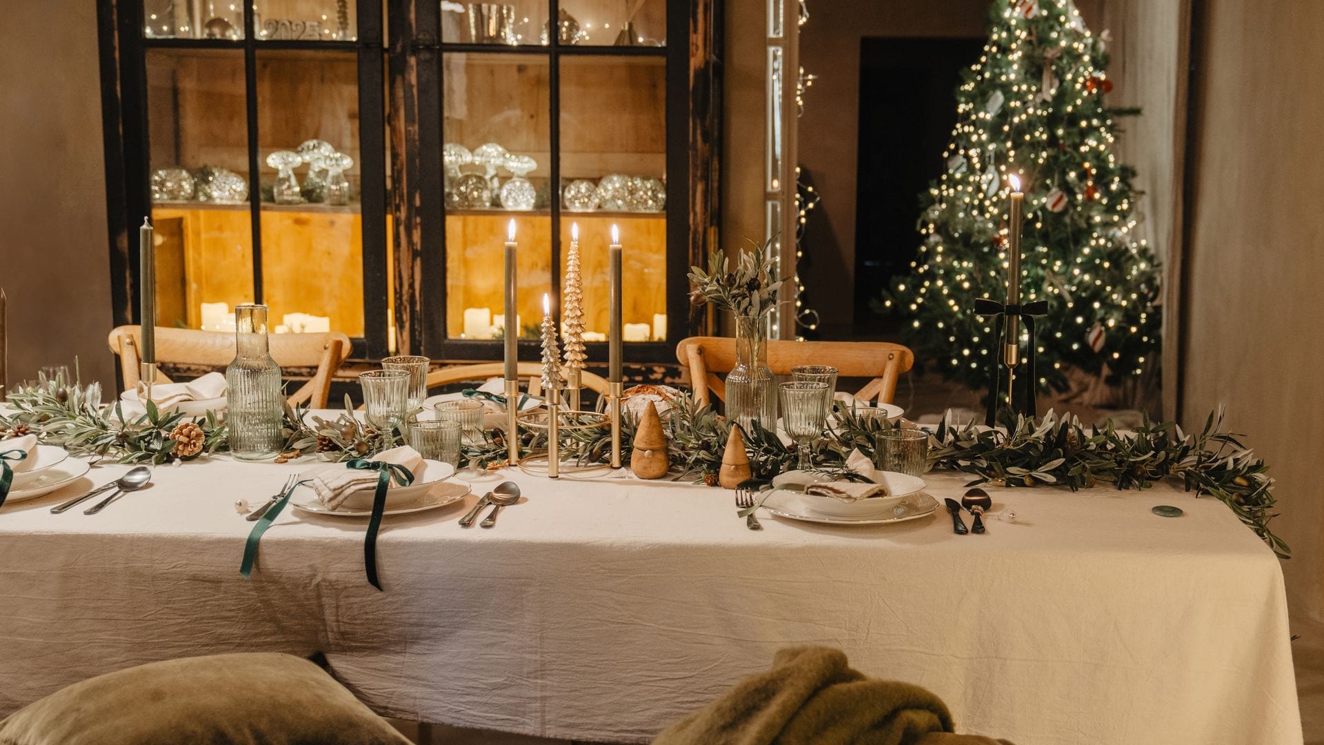 Mesa de Navidad con árbol, mantel blanco, vajilla blanca, candelabros uy vitrina iluminada