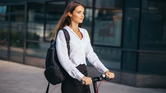 Mujer con camisa, falda tubo y mochila en un patinete eléctrico