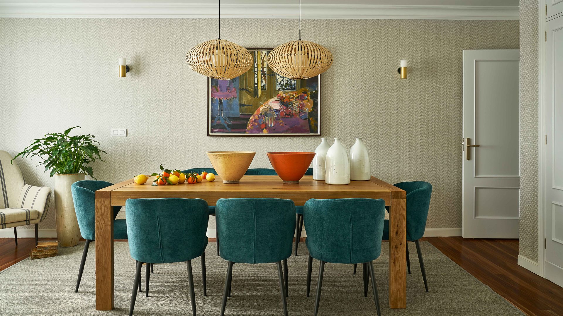 Comedor con mesa de madera, sillas tapizadas en azul, lámparas de techo de fibras, adornos en la mesa y cuadro en la pared