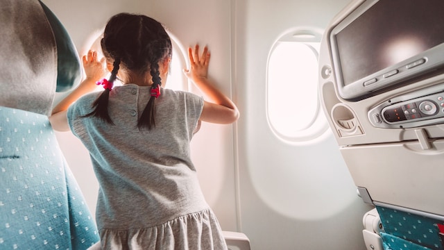 Lovely little girl kneel down on the aeroplane seat, and leaning on the aeroplane's window looking outside of the window, ready and waiting for take off curiously.