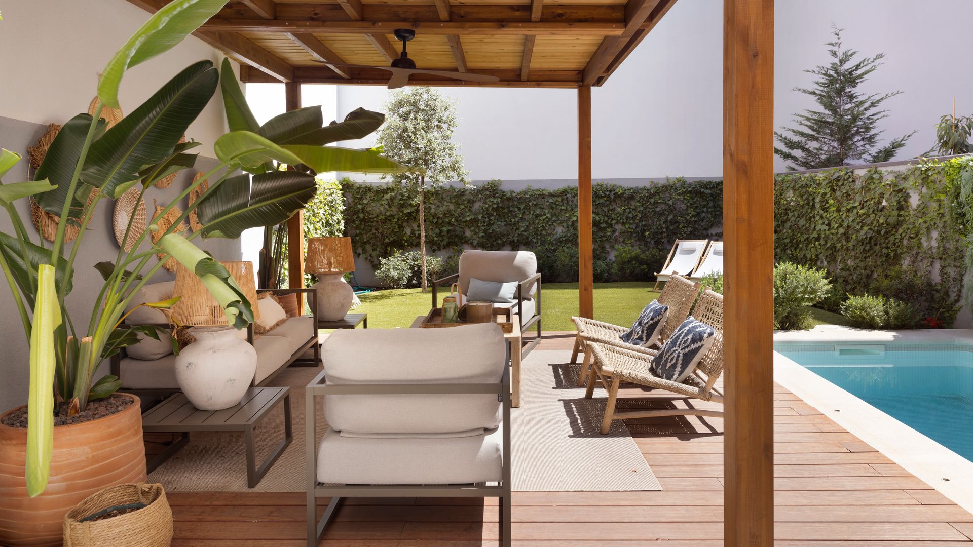 Porche con pérgola de madera, estar con butacas y hamacas, piscina y jardín