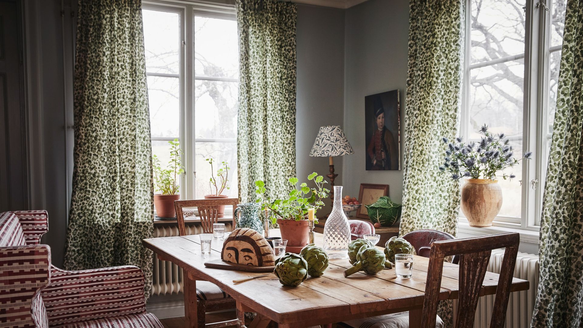 Comedor de estilo cottage con mesa de madera, sillón y cortinas de flores 