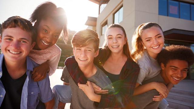 Adolescentes en el patio del instituto llevándose unos a otros a cuestas