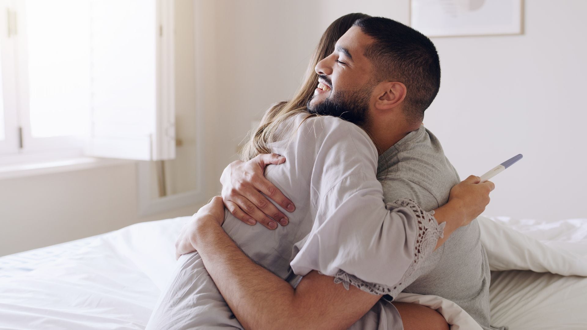 Pareja se abraza feliz tras ver el resultado de un test de embarazo