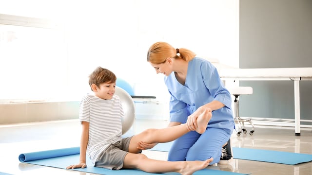Niño en consulta de fisioterapia haciendo ejercicios con la pierna