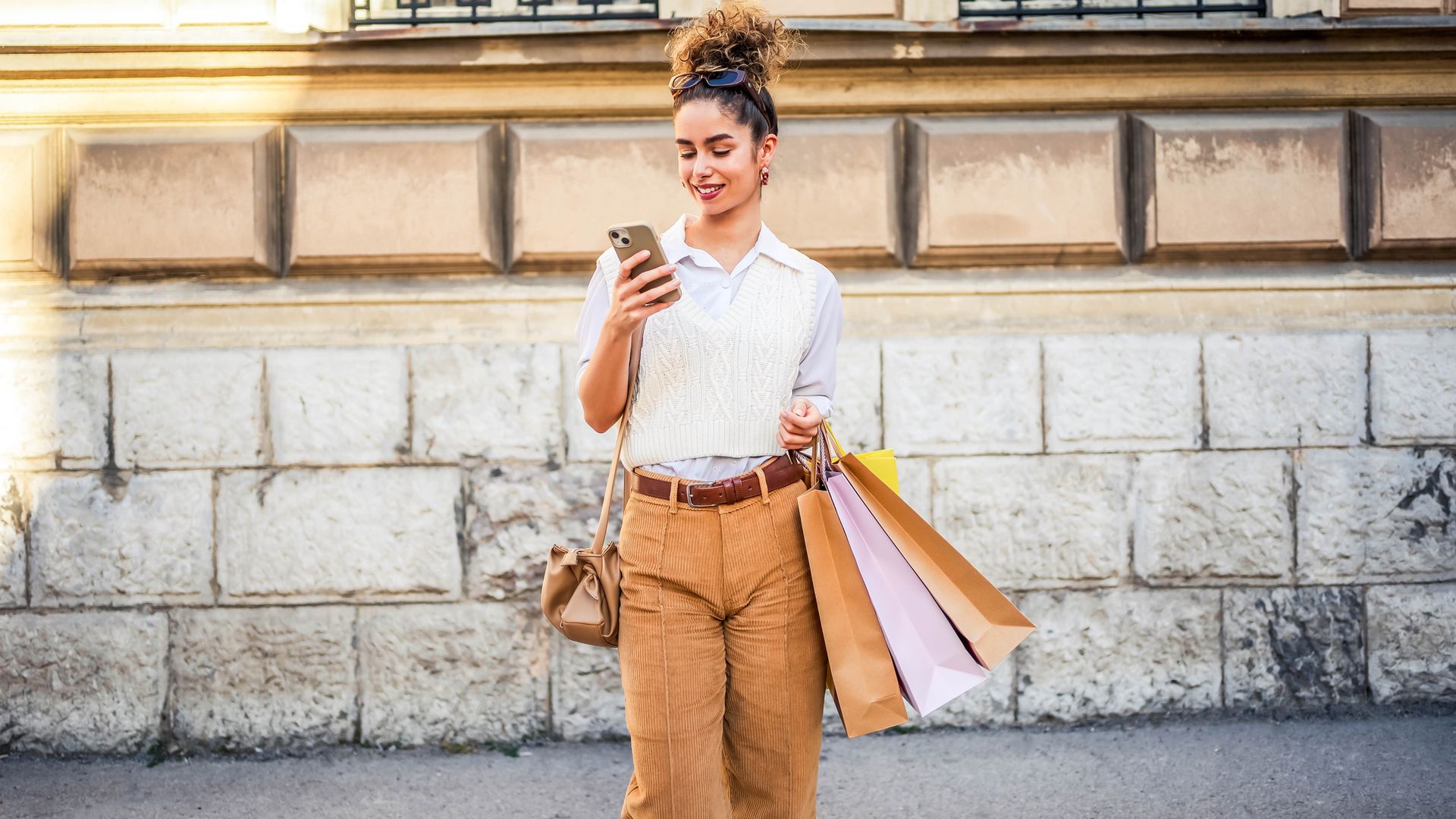 Mujer mirando su teléfono móvil en la calle con bolsas de compras