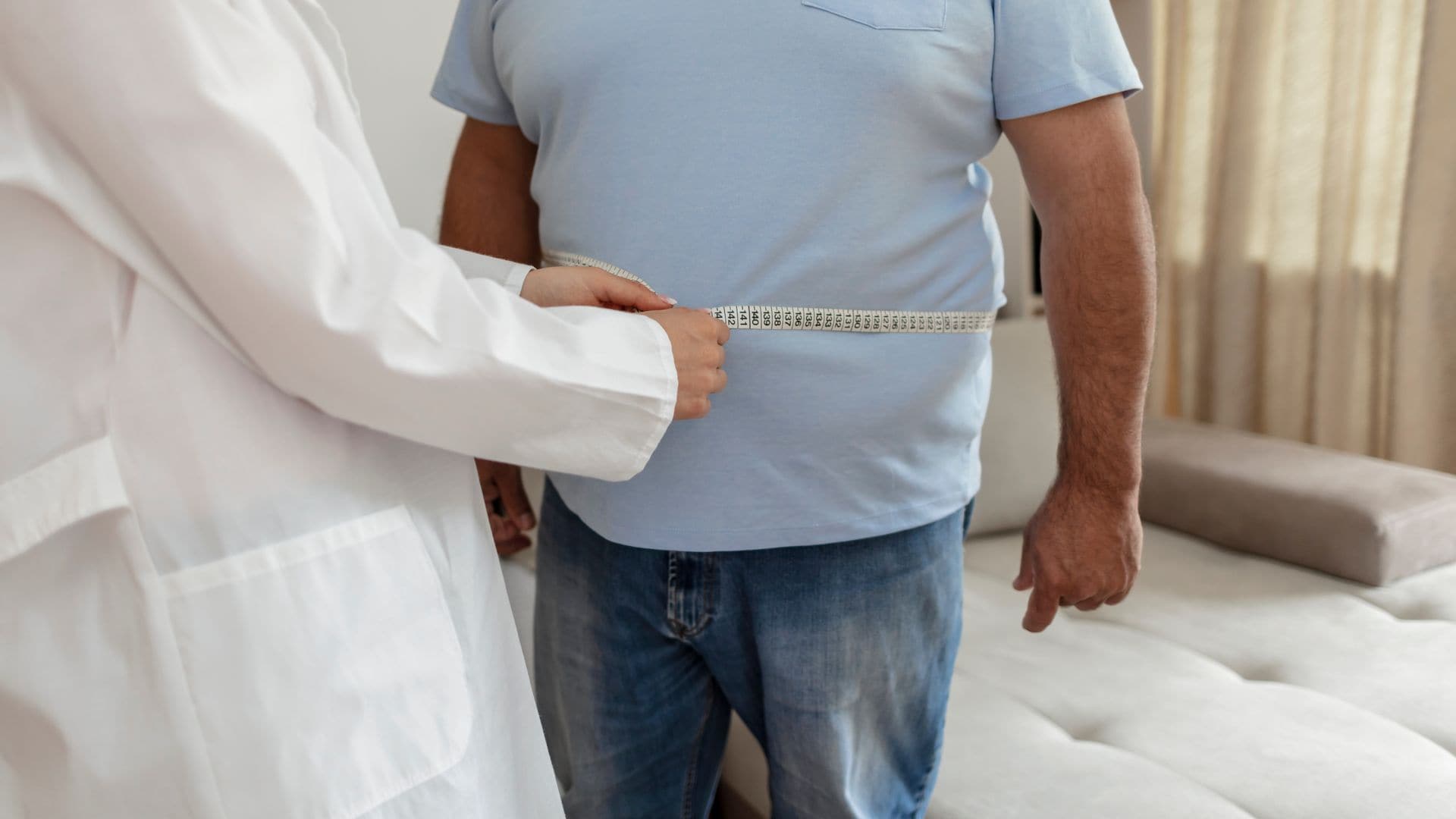 Un médico nutricionista mide el cuerpo de un paciente masculino con una cinta métrica sobre el tejido adiposo y el exceso de peso. 