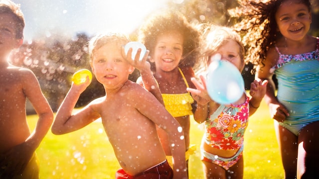 Niños felices jugando con globos de agua en el jardín en verano
