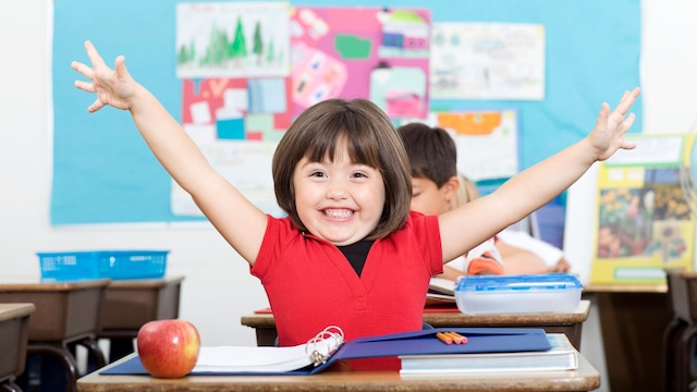 Niña sentada en su pupitre en clase sonríe muy feliz