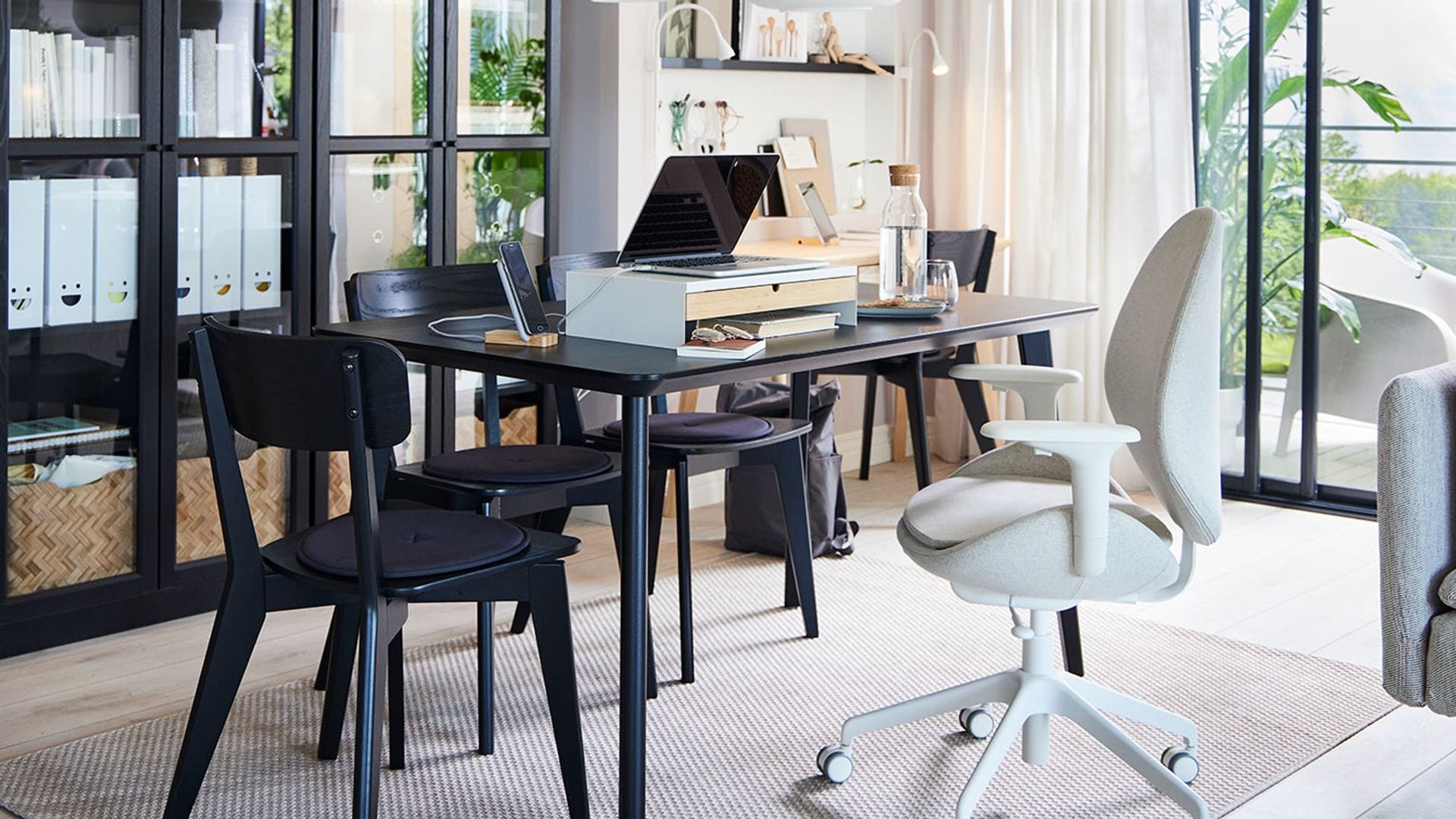 Salón IKEA con mesa negra de oficina, silla ergonómica y librería negra con puertas de cristal 