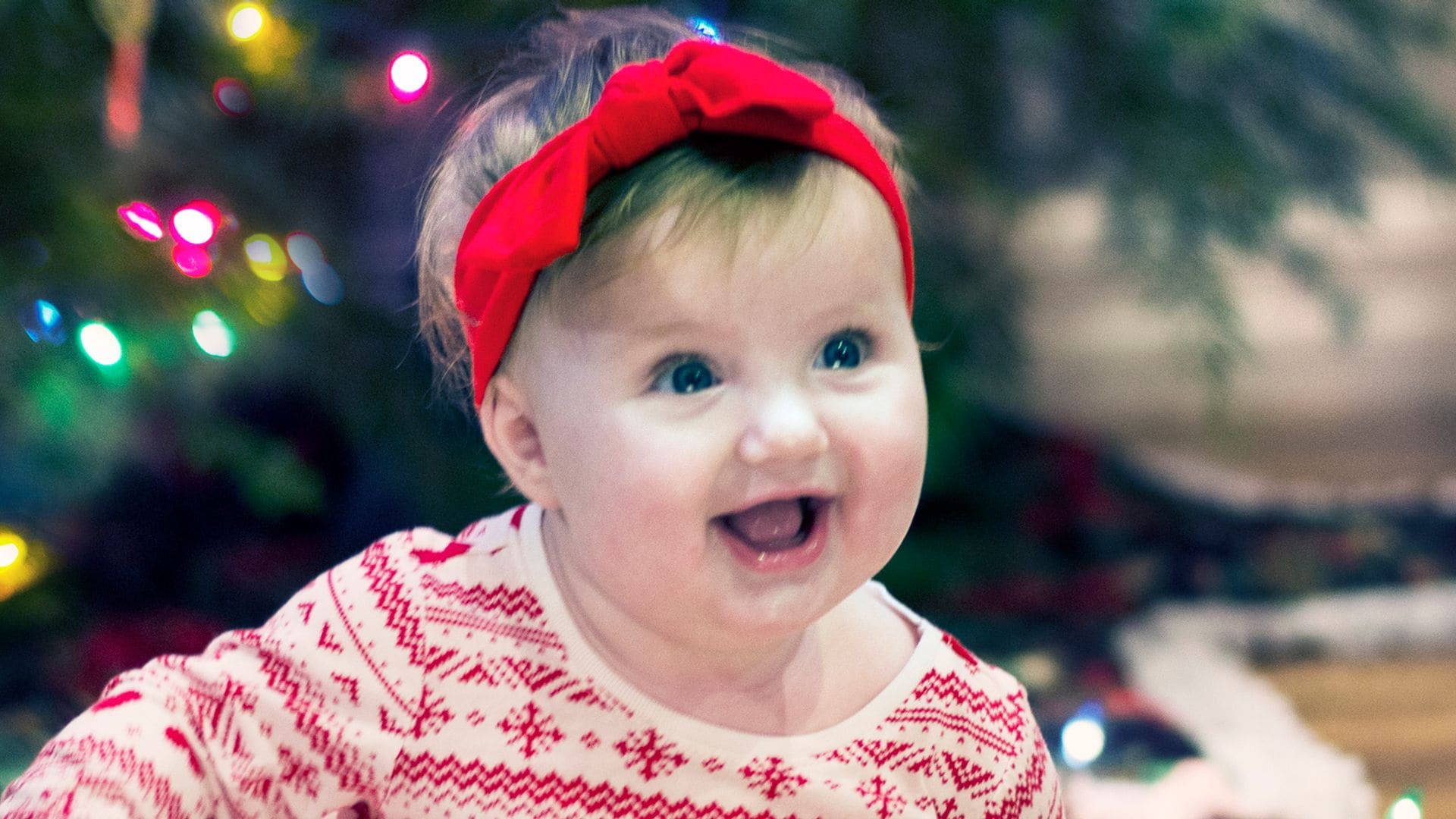 Bebé niña sonríe junto al árbol de Navidad