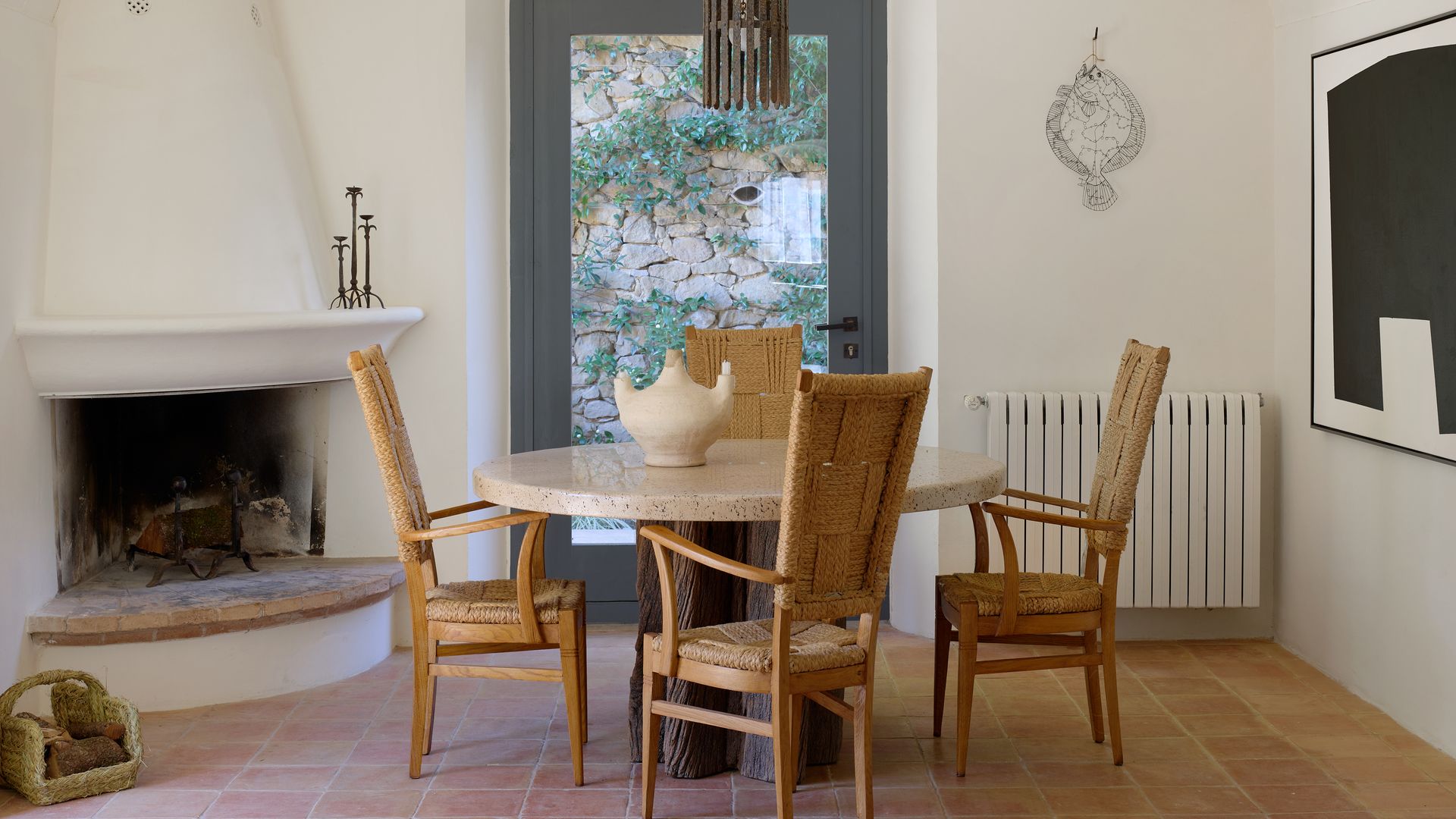 Comedor con chimenea en casa de campo, suelo de barro y sillas de fibras vegetales