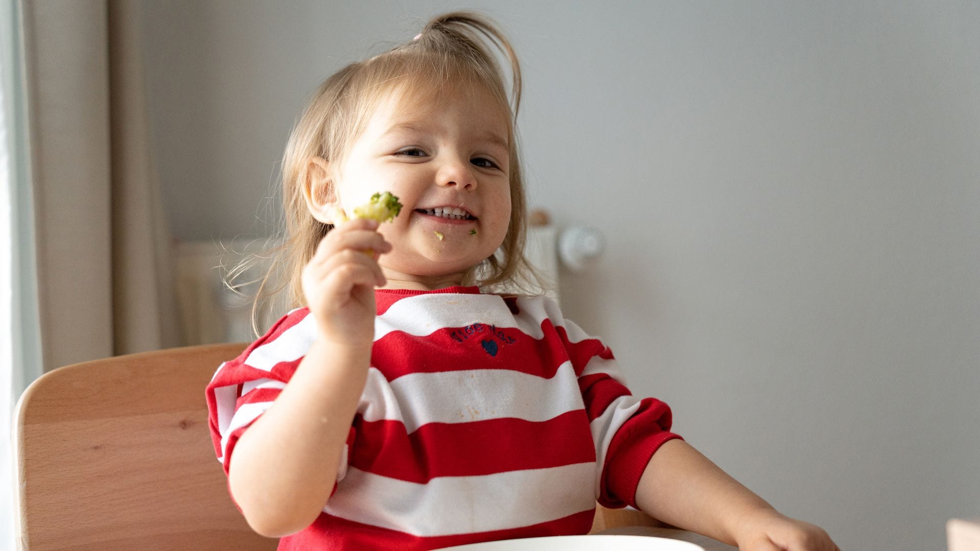 Niña come brócoli y sonríe