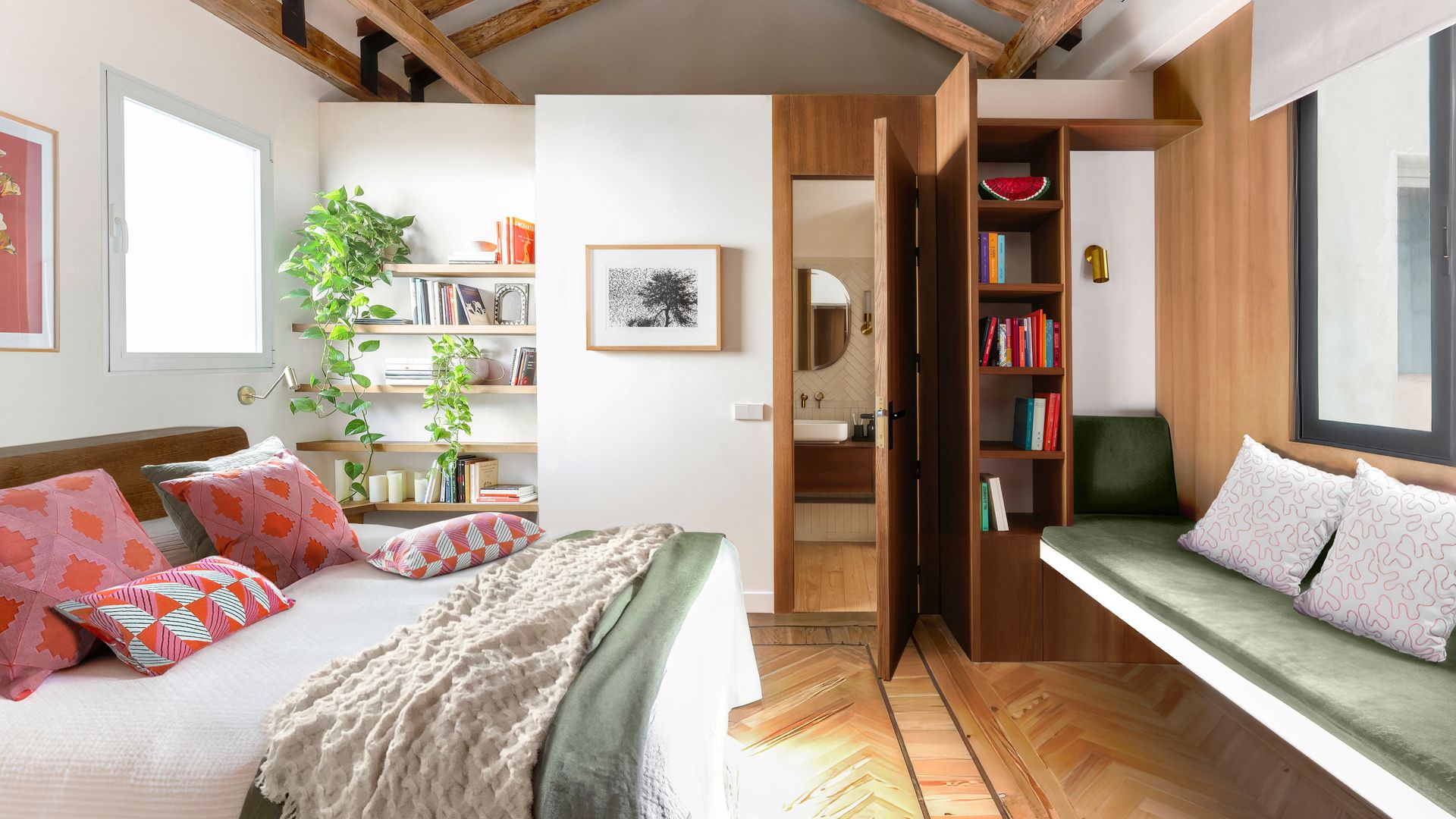 Dormitorio con vigas de madera en el techo, baldas con libros y estantería, banco con librería y suelo de madera en espiga