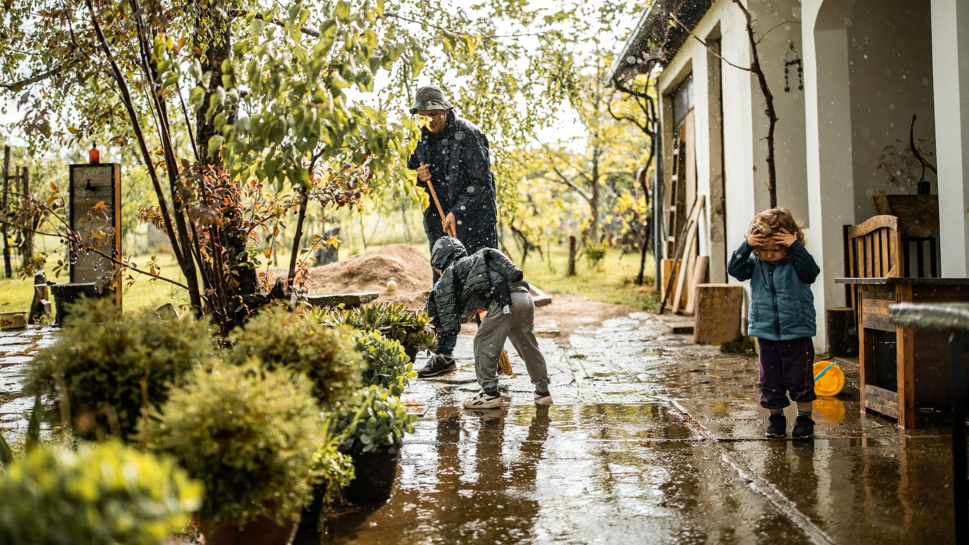 Son helping father and sweeping water from front yard on rainy day