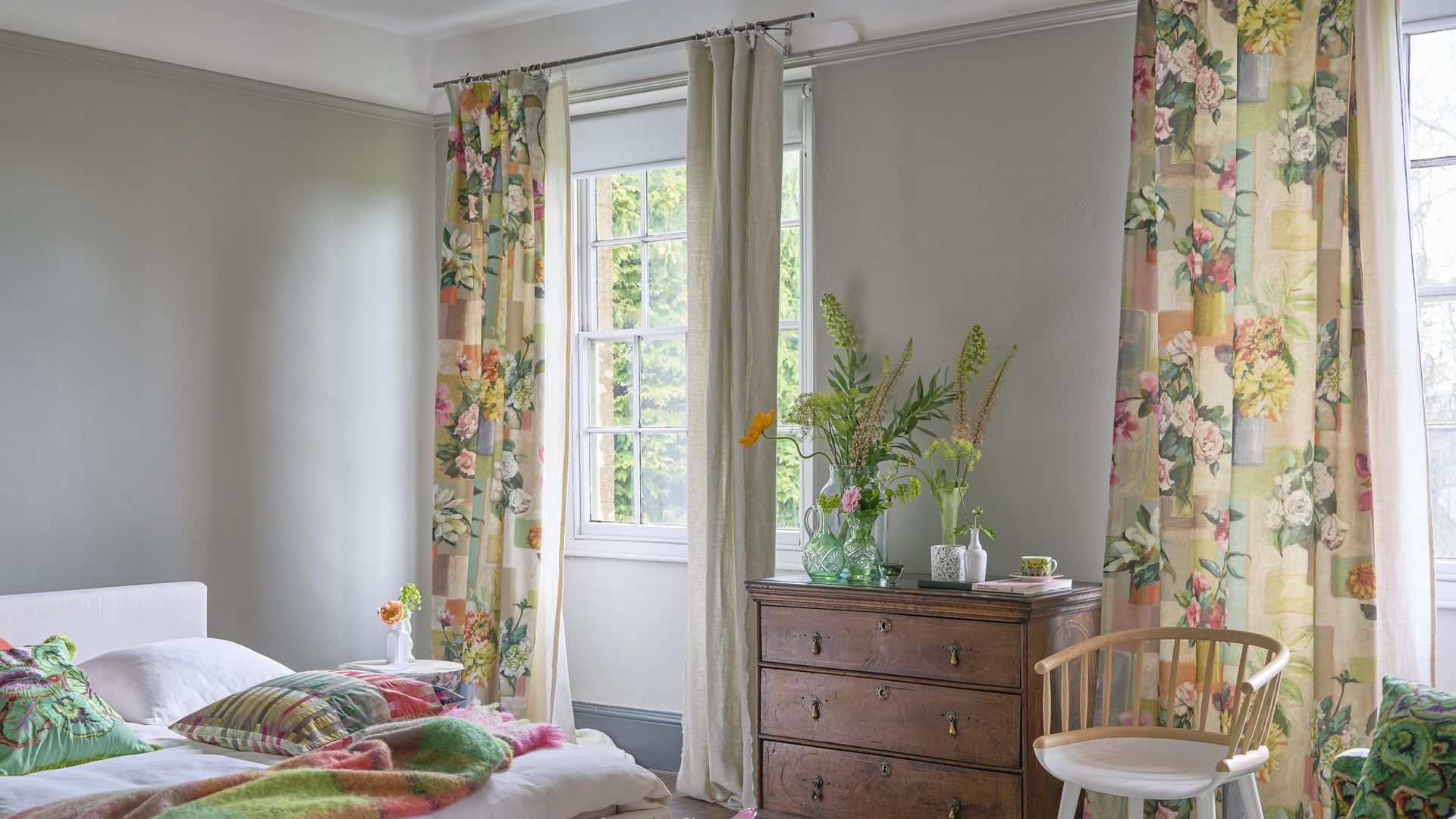 Dormitorio con cortinas de flores, ropa de cama verde y rosa, cómoda de madera y arreglos florales