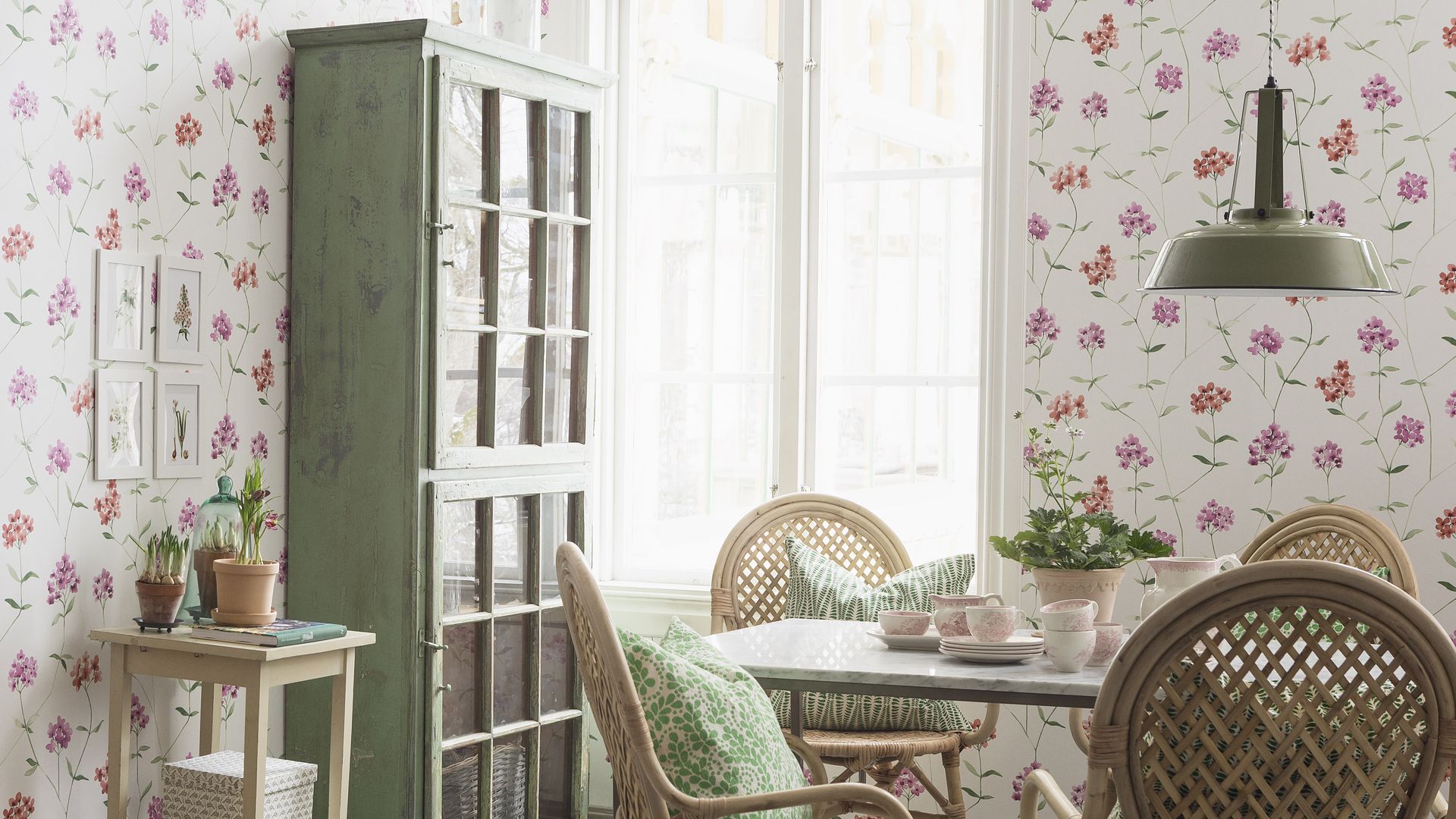 Comedor con papel pintado de flores, mesa de madera, sillas de fibras vegetales y alacena de madera verde 