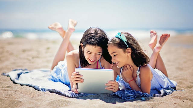 Dos niñas miran sonrientes una tablet en la playa