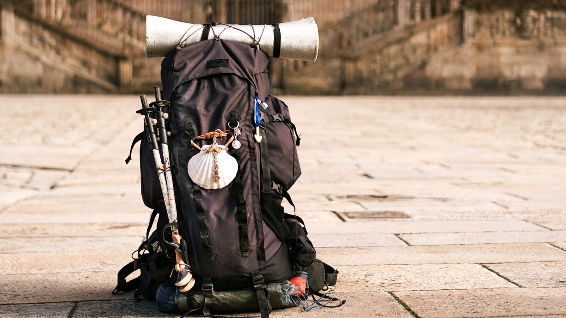 Pilgrim's rucksack resting on the ground in front of the door of Santiago de Compostela's holy cathedral. Walking sticks, shell, sleeping mat.