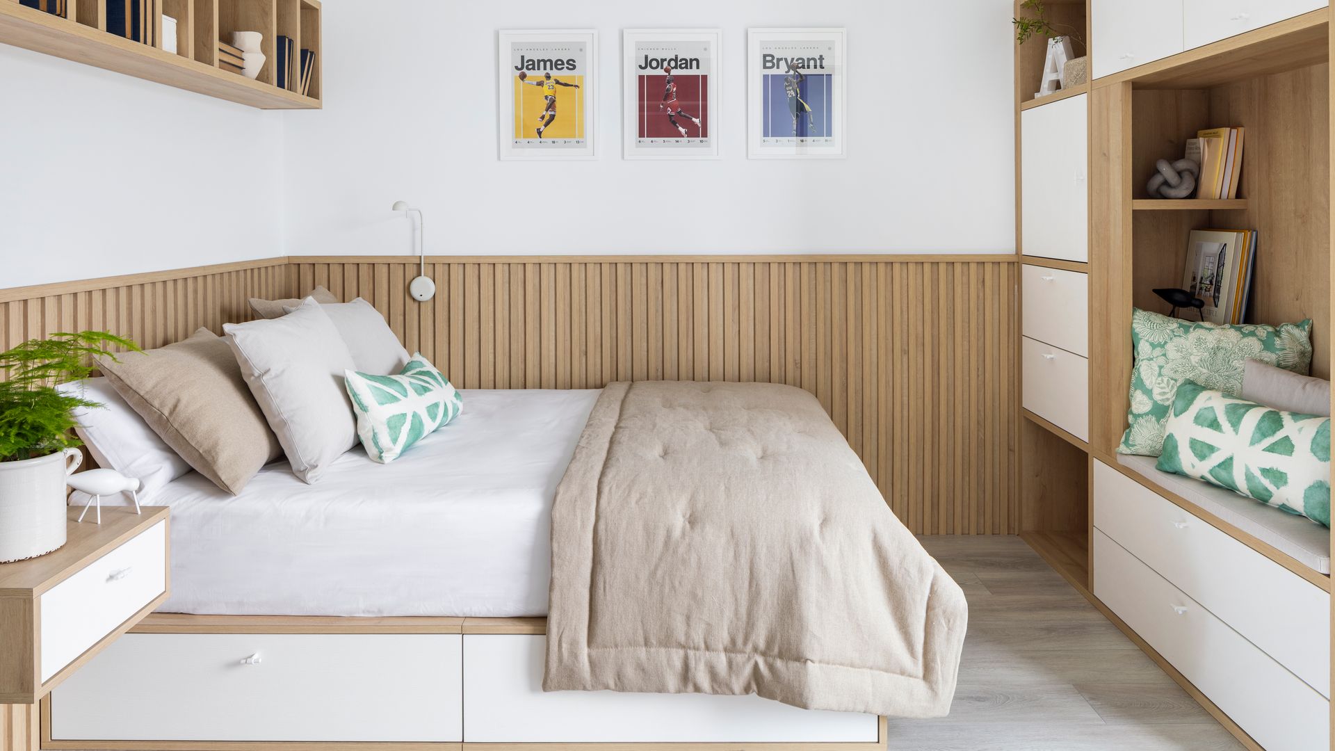 Dormitorio con zócalo alto de lamas de madera, cama con cojines y mueble a medida con blanco y cajones