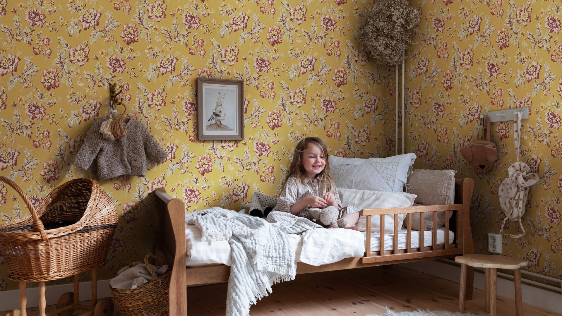 Habitación infantil con papel amarillo de flores, cama de madera, niña y alfombra