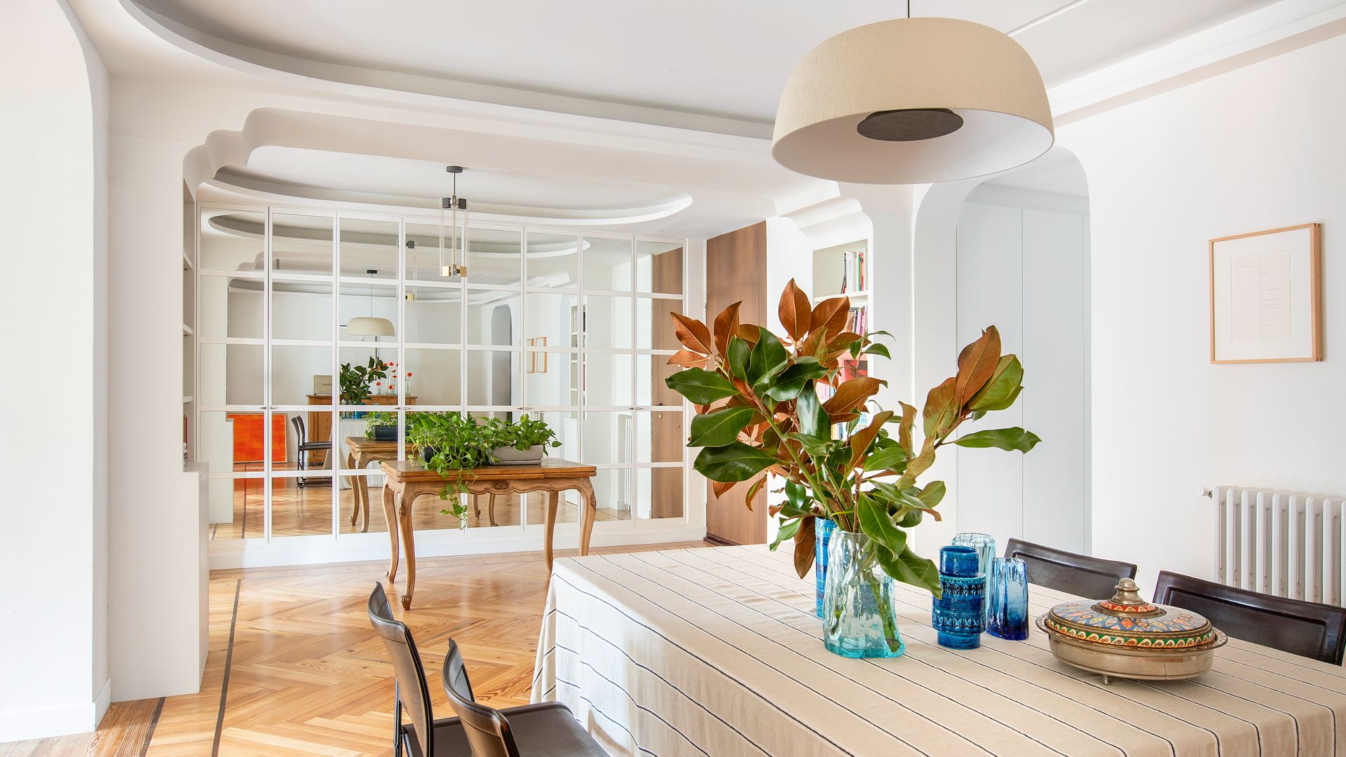 Comedor con pared de espejo con cuarterones blancos, mesa con mantel y lámpara de techo