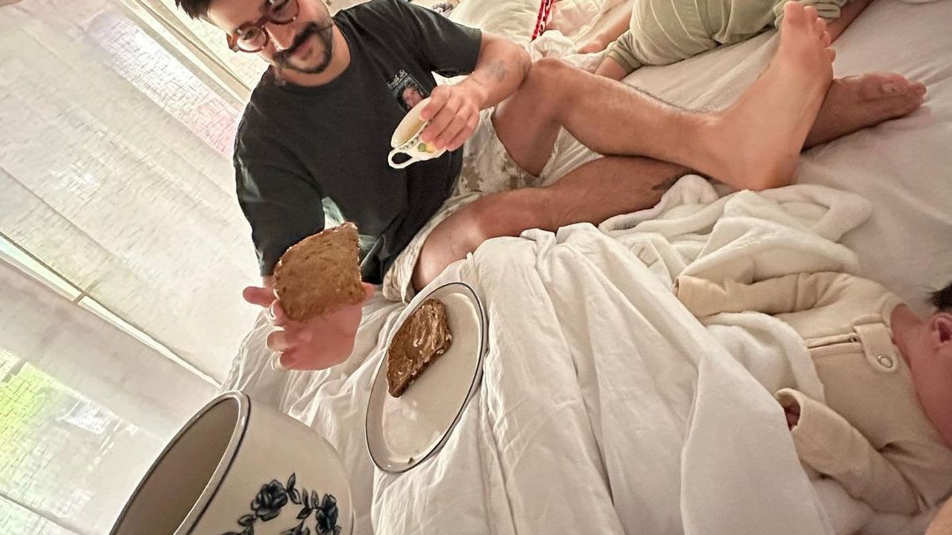 Los orgullosos padres haciendo un pícnic de café y tostadas en la cama con su bebé