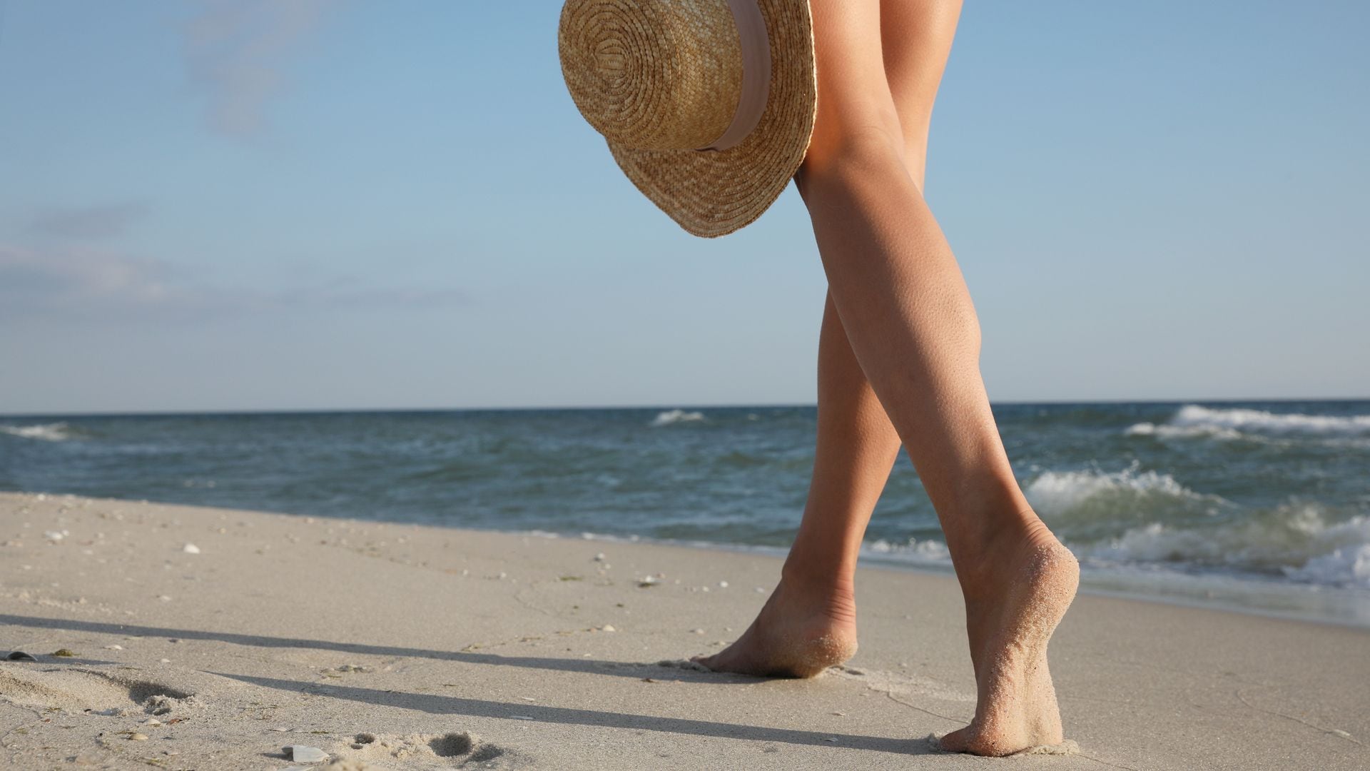 mujer caminando por la arena de la playa descalza con un sombrero en la mano