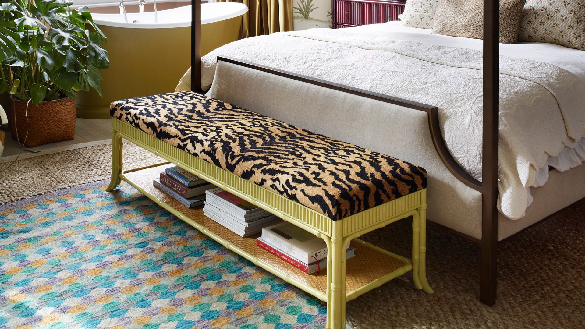 Dormitorio con bañera exenta amarilla, cama con dosel, pared con papel pintado de flores, banqueta con asiento animal print, alfombra y planta