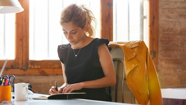 Mujer en la oficina escribiendo sobre un cuaderno de notas.